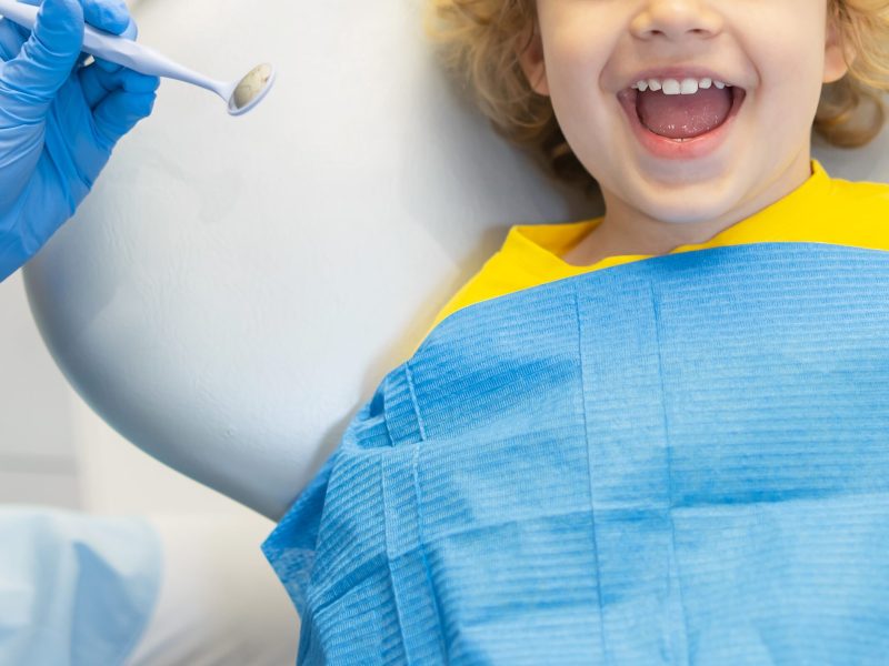 Cute young boy visiting dentist, having his teeth checked by female dentist in dental office.